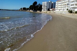 Ein Strand mit sandigem Ufer, ruhiger See und eine Reihe weißer Gebäude mit Balkonen.