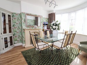 A dining area with a glass table, metal chairs, a green patterned rug, a white vase with flowers, and a fireplace. - Laburnum House (Ellesmere Port)