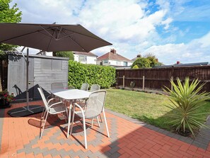 An outdoor patio with a table and chairs, a large umbrella, and a brick pathway. - Laburnum House (Ellesmere Port)