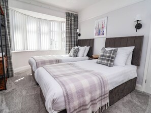 A bedroom with two beds, a window with blinds, a wall-mounted lamp, and a framed picture. - Laburnum House (Ellesmere Port)