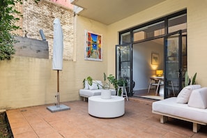 A modern outdoor seating area with a white sofa, a round table, and potted plants. - Riley Escape Walkable City Living with Courtyard (Surry Hills)