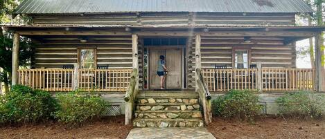 A rustic log cabin with a stone entrance, wooden porch, and a metal roof.