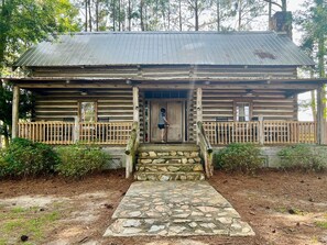 A rustic log cabin with a stone entrance, wooden porch, and a metal roof. - Presley Deluxe Log Cabin (Hartsfield)