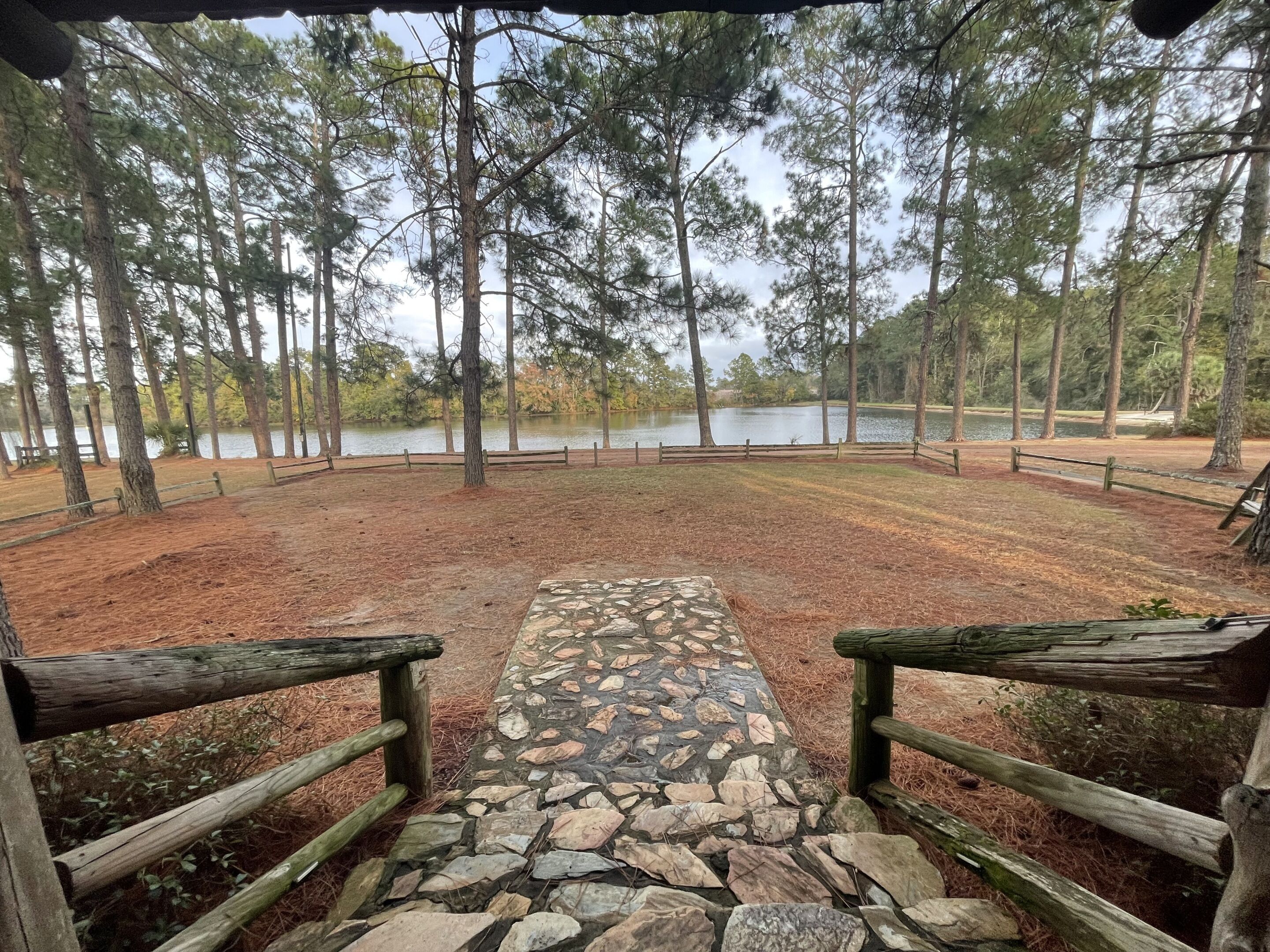 A stone pathway leading to a wooden deck with a view of a lake surrounded by trees.