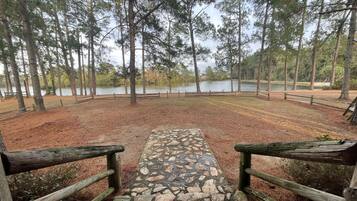 A stone pathway leading to a wooden deck with a view of a lake surrounded by trees.