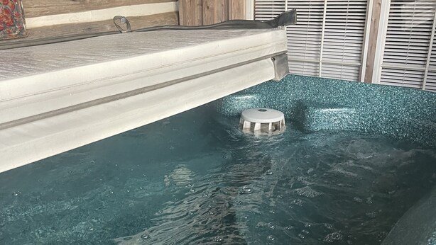 A hot tub with a built-in seat, surrounded by wooden walls and a window with blinds.