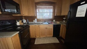 A compact kitchen with wooden cabinets, a microwave, stove, sink, and a refrigerator.