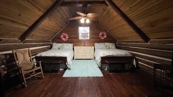 A log cabin bedroom with two beds, a dresser, a rocking chair, and a ceiling fan.