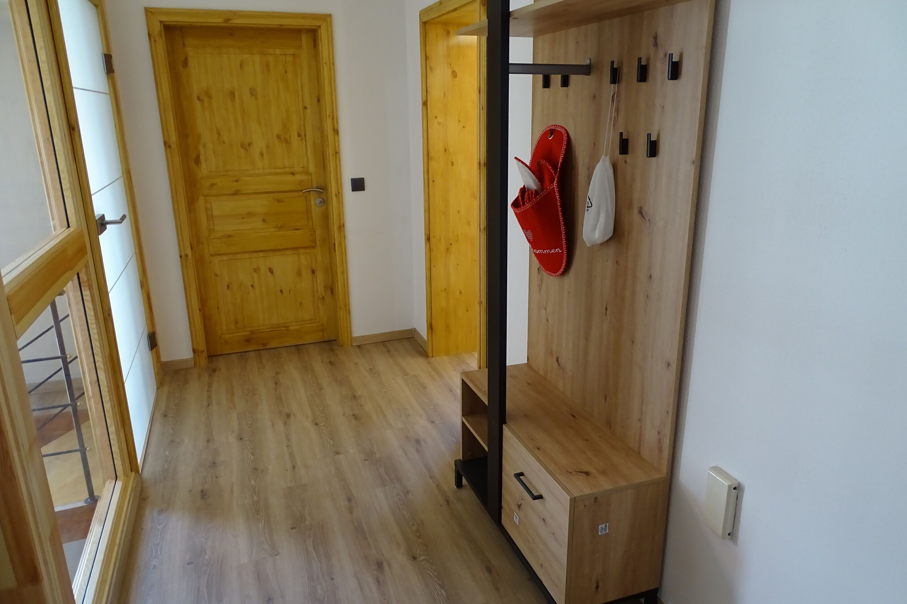 A hallway with wooden flooring, a wooden door, and a coat rack with a red item on it.