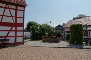 Ein Innenhof mit Kopfsteinpflaster, ein traditionelles Fachwerkhäuschen und ein Blumenbeet mit rosa Blüten.