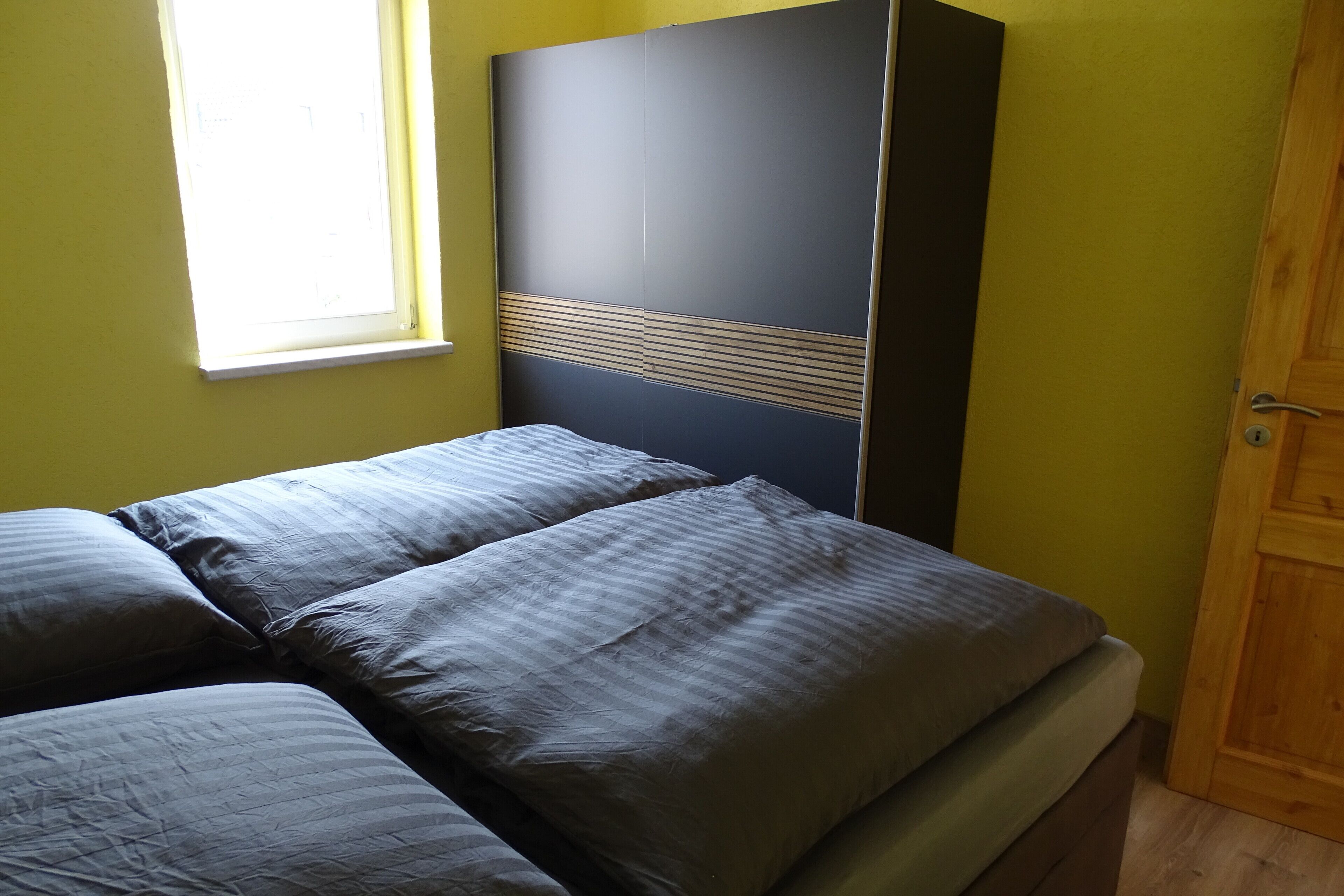 Una cama con ropa de cama gris en una habitación con paredes amarillas y una ventana.