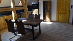 A dining area with a wooden table and chairs, a kitchen with appliances, and a wooden door. - Family-Friendly Vacation Rental (65 m²) Near the Vessertal Nature Reserve (Schleusingen)