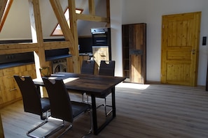Ein Essbereich mit Holztisch und -stühlen, eine Küche mit Geräten und eine Holztür.