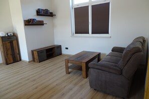 Ein Wohnzimmer mit Holzboden, einer Couch, einem Couchtisch, einer TV-Konsole und zwei Bücherregalen.