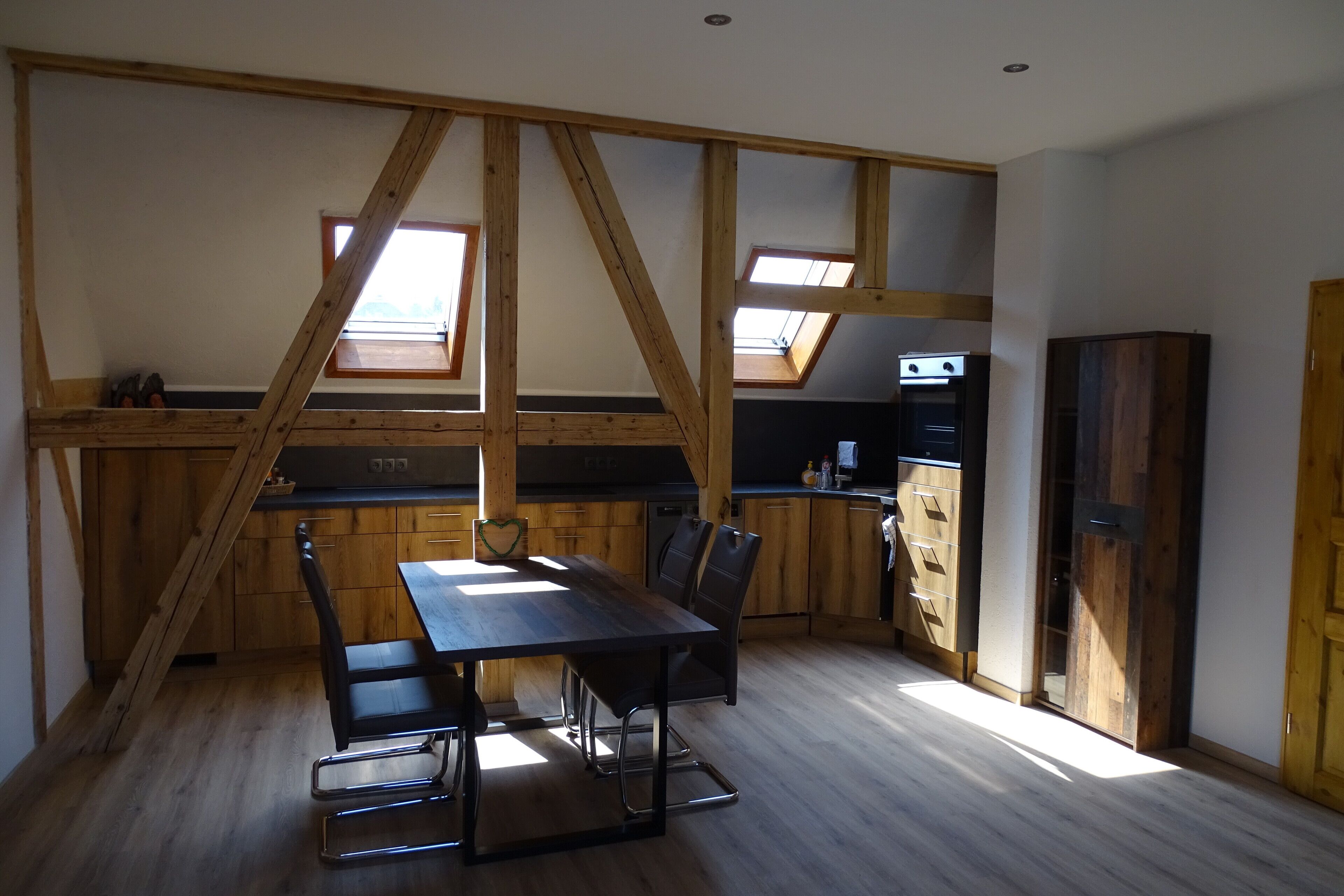 A kitchen with wooden beams, a dining table with chairs, and a built-in oven.