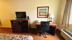 Een hotelkamer met een bureau, stoel, bed en een schilderij aan de muur.