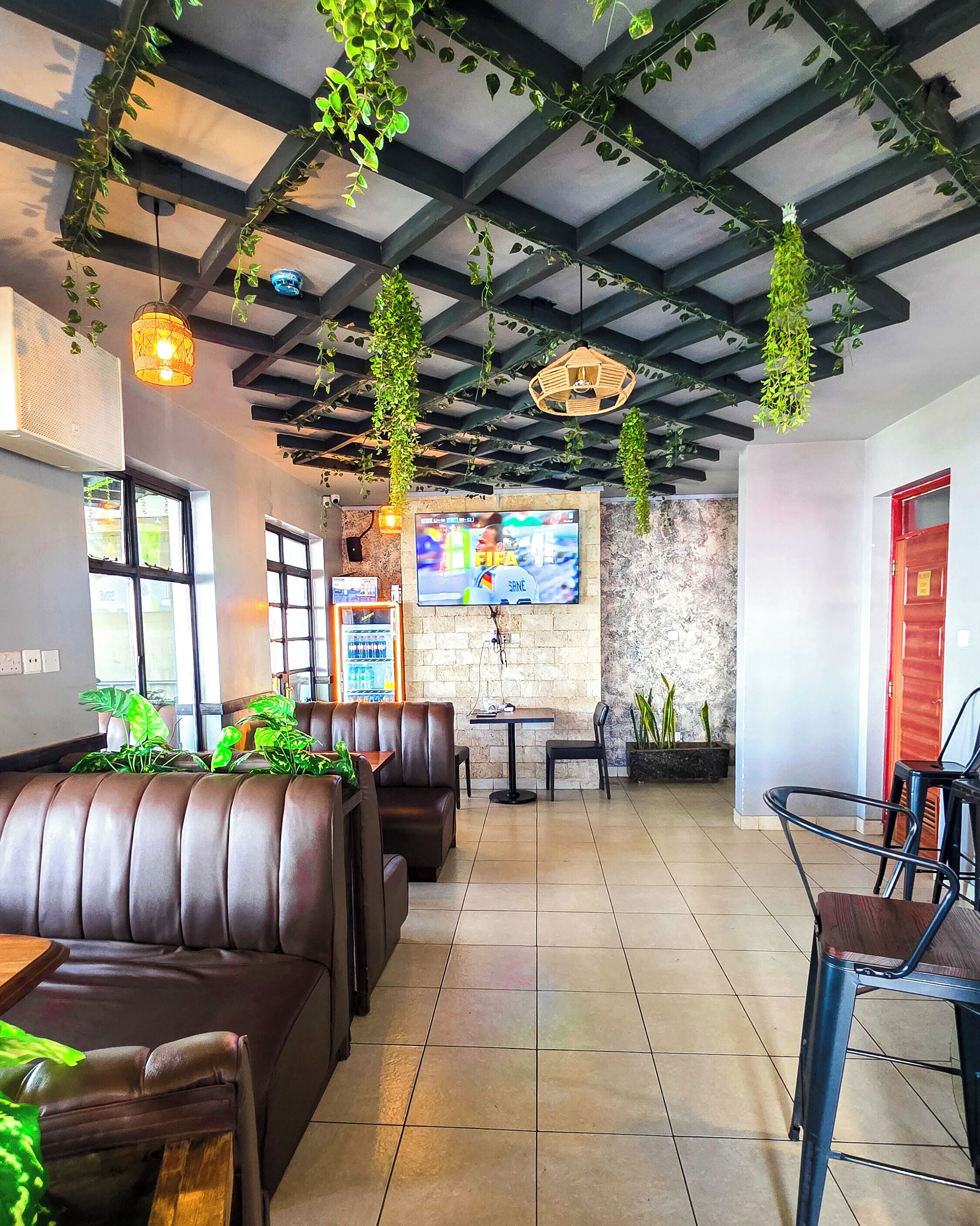 A restaurant interior with booths, hanging plants, a TV screen, and a tiled floor.