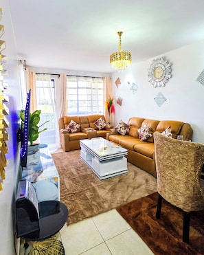 A living room with a sofa set, a coffee table, a TV, and decorative wall art. - 3BR Luxury Retreat in Tatu City,Family& Business Stay (Wilaya ya Kiambu)