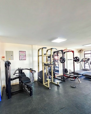 Ein Fitnessraum mit verschiedenen Trainingsgeräten, darunter eine Hantelbank, ein Squat-Gestell und ein Laufband.