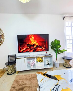 Un salon doté d’un téléviseur à écran plat diffusant une image de cheminée, d’un meuble de rangement blanc, d’une grande plante verte et d’une table basse en marbre.