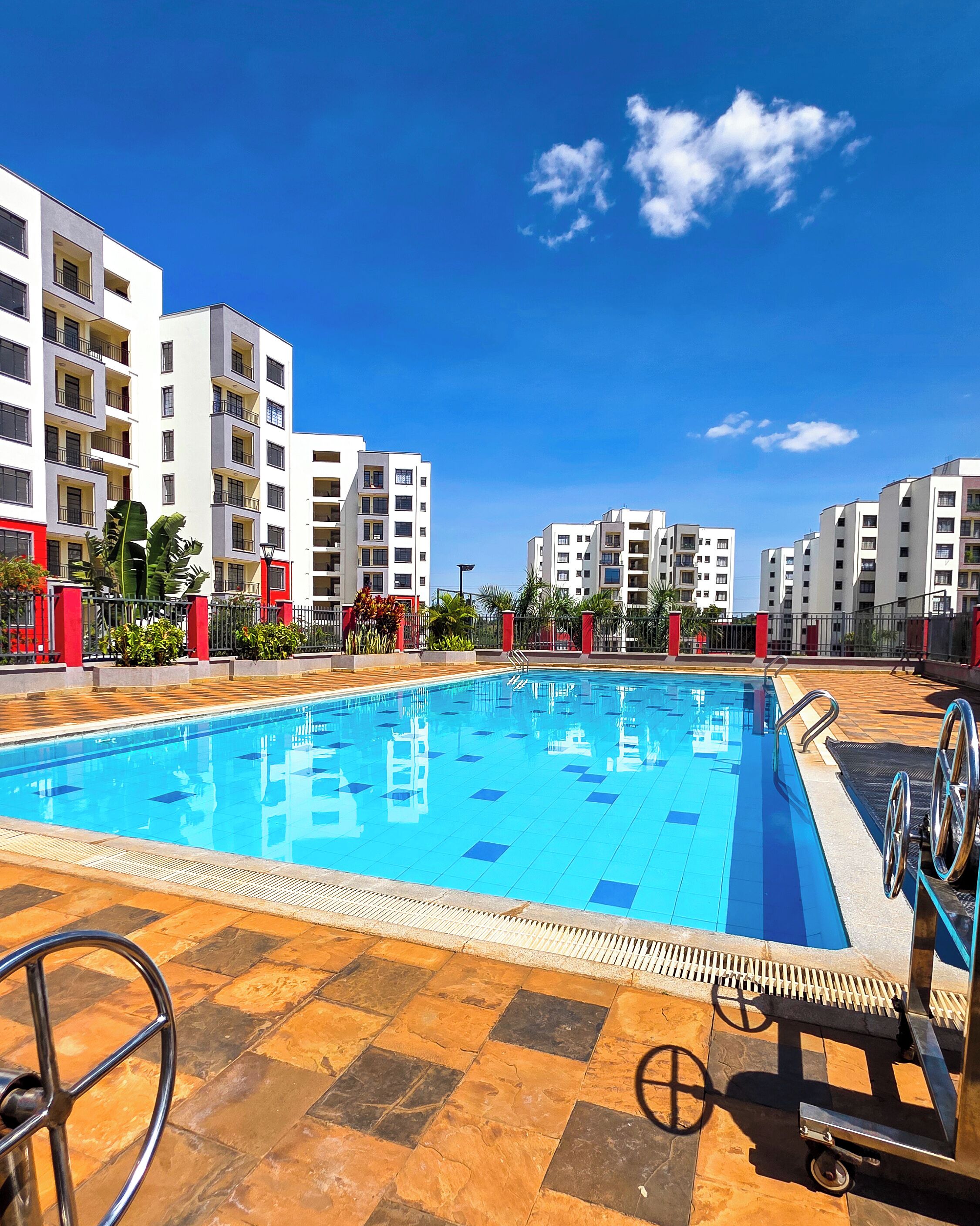 Une piscine dotée d’une plage carrelée, entourée d’immeubles résidentiels à plusieurs étages.