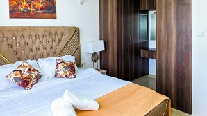 Een hotelkamer met een groot bed, een hoofdeinde, een schilderij, een kledingkast en een spiegel in de badkamer.