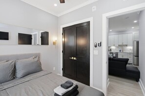 Um quarto moderno com uma cama, uma porta escura, um pequeno espaço de estar e vista para uma cozinha.