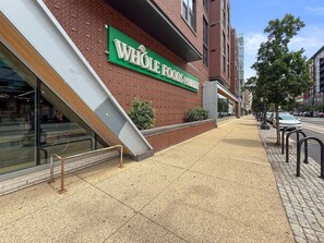 Um Whole Foods Market com fachada de tijolos, uma entrada visível e uma calçada com barreira de metal.