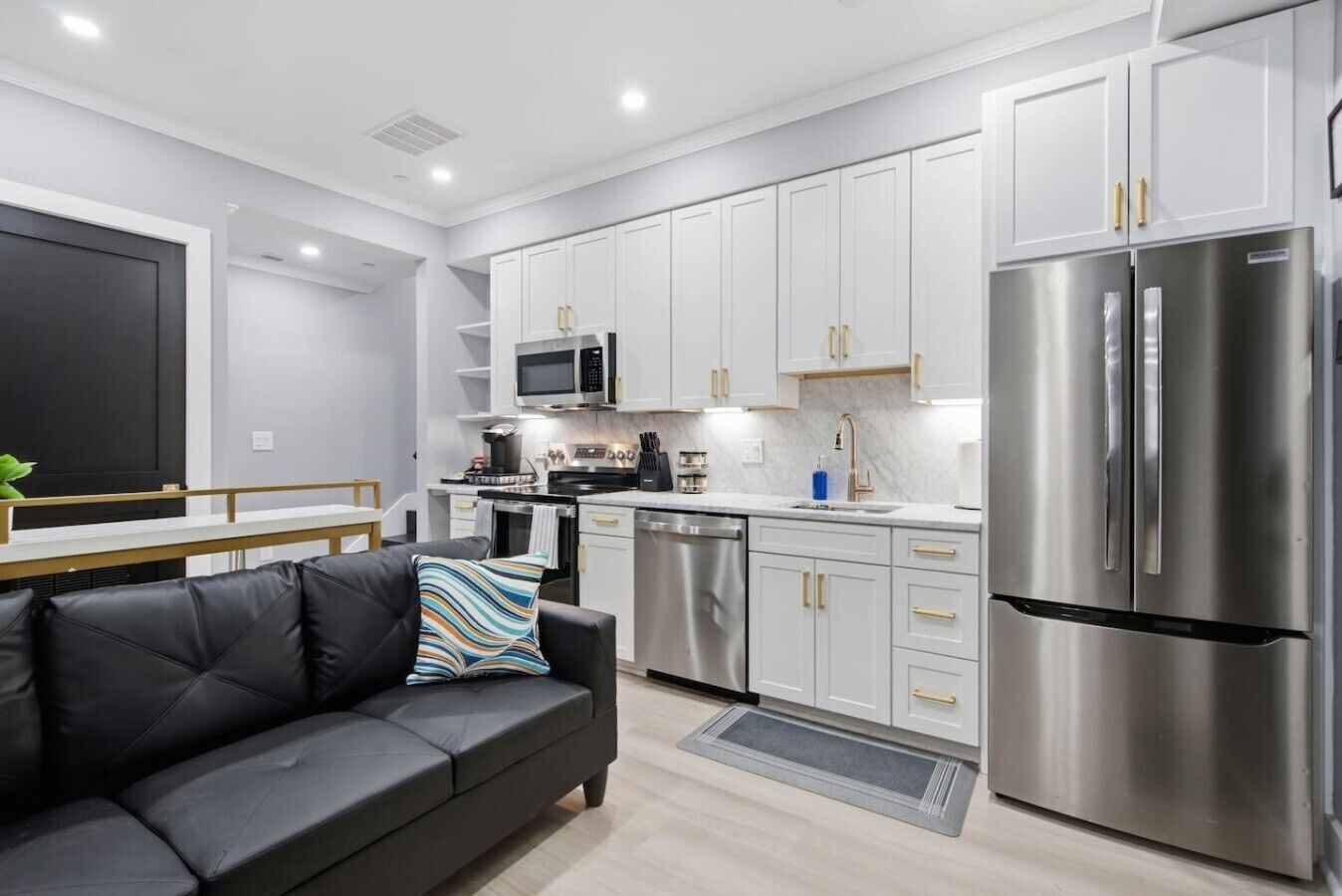 A modern kitchen with white cabinets, stainless steel appliances, and a black leather sofa with a striped pillow.