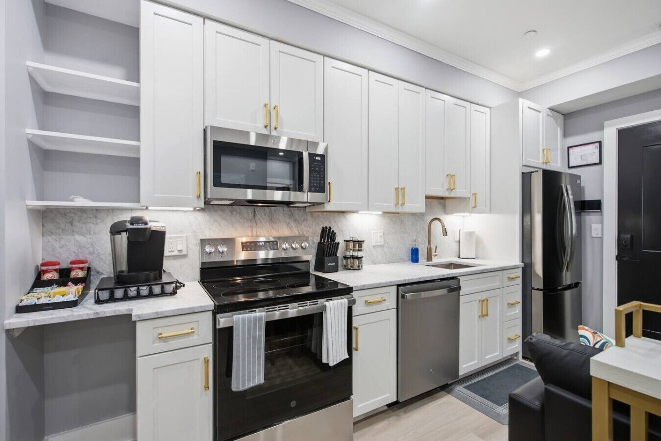 Una cocina moderna con muebles blancos, electrodomésticos de acero inoxidable y una cafetera.