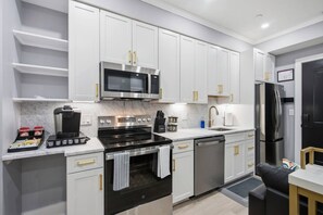 A modern kitchen with white cabinetry, stainless steel appliances, and a coffee machine.