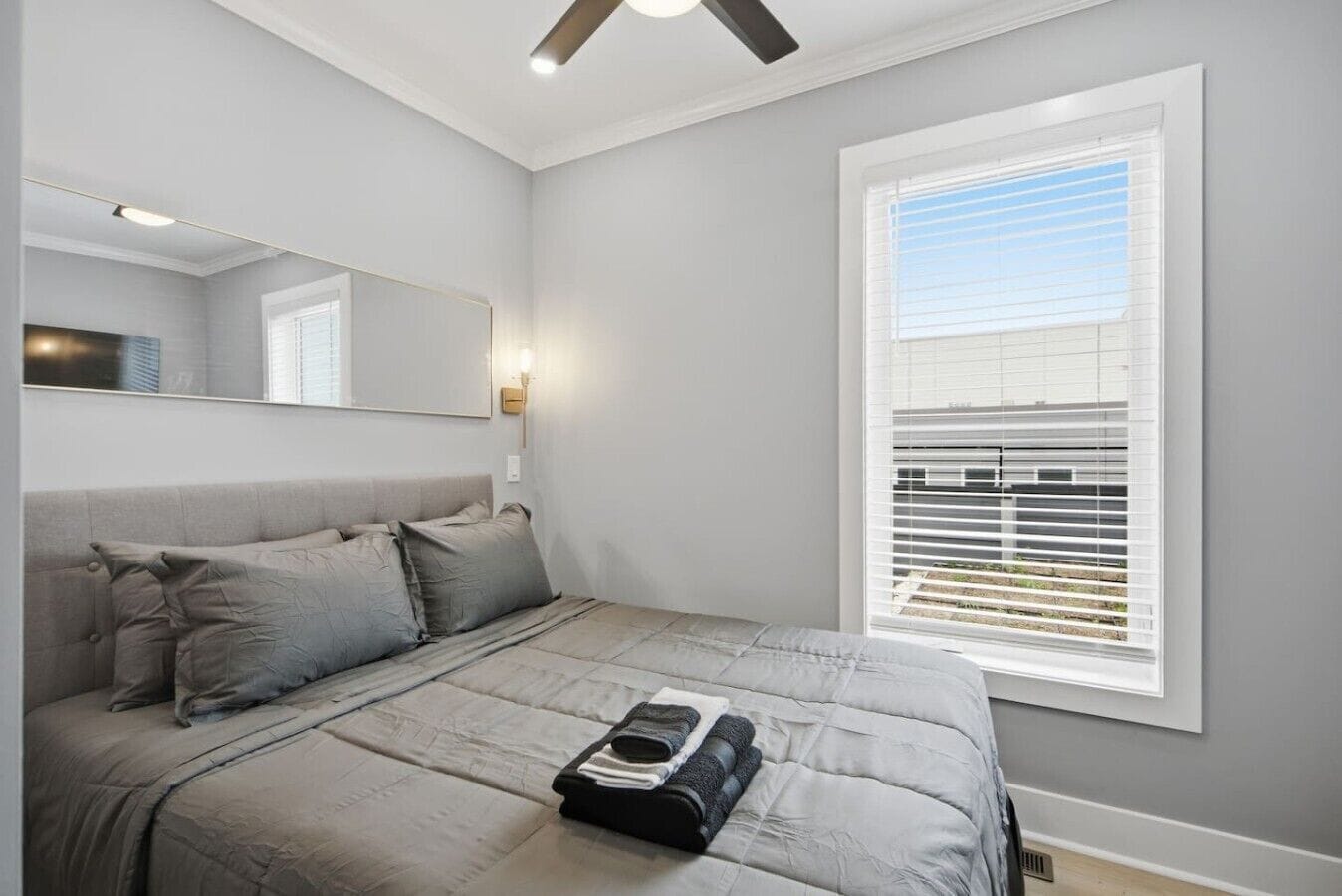 Un dormitorio con cama, mesita de noche, espejo y ventana con persianas.