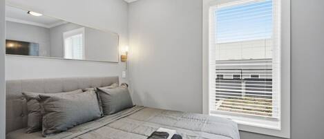 Un dormitorio con cama, mesita de noche, espejo y ventana con persianas.