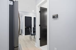 Un couloir donnant sur un espace cuisine moderne, une table à manger avec des chaises et une porte noire.