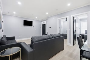 A modern living room with a sectional sofa, a glass coffee table, and a flat-screen TV mounted on the wall. - H Street Hideaway | Stylish 4BR in NE DC (Washington)