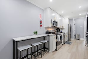 A modern kitchen with a marble countertop, stainless steel appliances, and a small bar area. - H Street Hideaway | Stylish 4BR in NE DC (Washington)