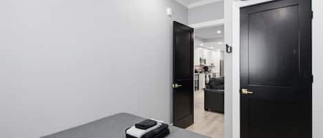 Une chambre à coucher avec un lit, une valise et une porte donnant sur une petite cuisine.