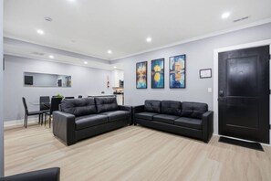 Ein modernes Wohnzimmer mit zwei schwarzen Ledersofas, einem Essbereich mit Tisch und Stühlen sowie einer Küche im Hintergrund.