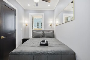 Ein Schlafzimmer mit einem Bett, Nachttischlampen, einer Tür und einem Fenster mit Jalousien.