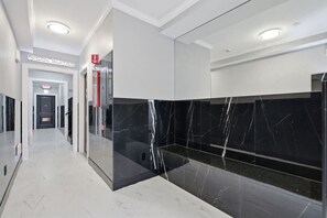 Ein moderner Hotelkorridor mit Glastrennwand, einem Schild mit der Aufschrift 'Nicol Suites' und einem Rauchmelder.