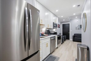 A modern kitchen with stainless steel appliances, white cabinetry, and a black sofa in the adjacent living area. - Historic H Street Haven | Modern 3BR, 1 Bath (Washington)