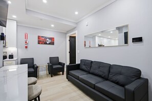 A modern living room with a black leather sofa, a small round table, two armchairs, and a painting on the wall. - Historic H Street Haven | Modern 3BR, 1 Bath (Washington)