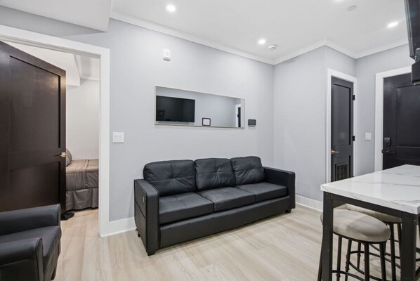 Ein modernes Wohnzimmer mit einer schwarzen Ledersofa, einem flachbildfernseher an der Wand und einem Essbereich mit einem Marmortisch.