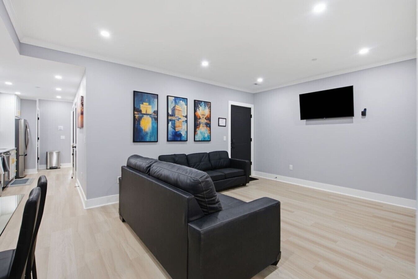Een moderne woonkamer met een modulaire bank, een flatscreen televisie aan de muur en een eethoek met een tafel en stoelen.