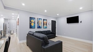 Un salon moderne avec un canapé d’angle, un téléviseur à écran plat fixé au mur et un coin repas comprenant une table et des chaises.