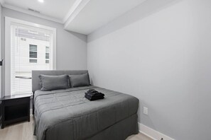 A bedroom with a bed, a bedside table, and a window with blinds.