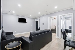 Een moderne woonkamer met een zwarte leren bank, een glazen salontafel en een flatscreen televisie aan de muur.