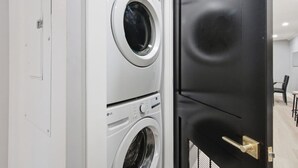 Une buanderie avec des machines à laver et des sèche-linge superposés, une porte noire et un mur blanc.
