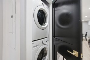 A laundry room with stacked washers and dryers, a black door, and a white wall.