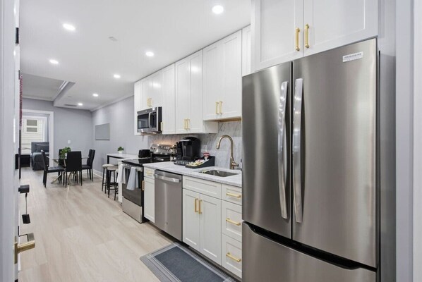 A modern kitchen with stainless steel appliances, white cabinetry, and a dining area with a table and chairs.